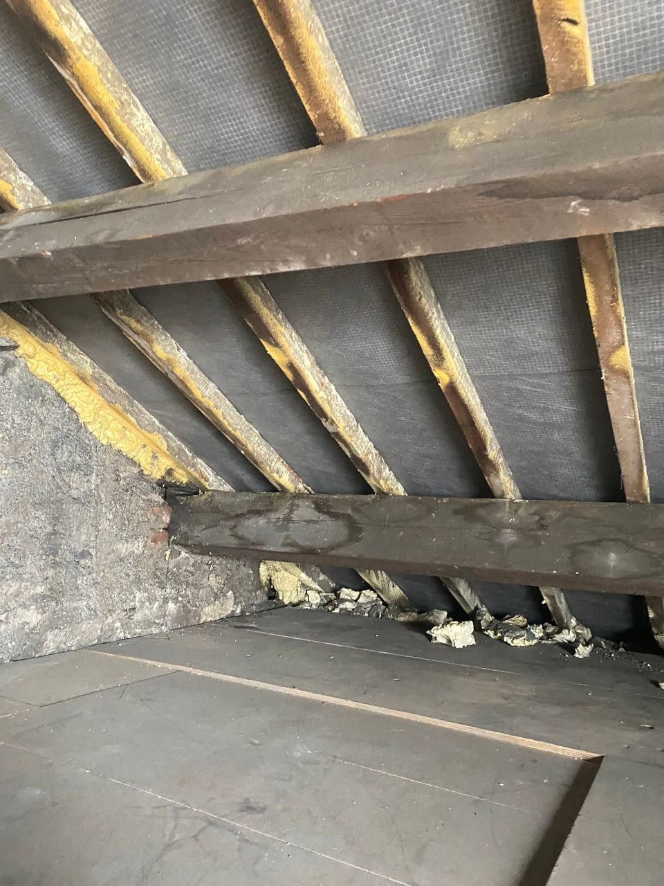 Loft rafters with residual closed-cell foam still bonded along both faces after a previous removal
