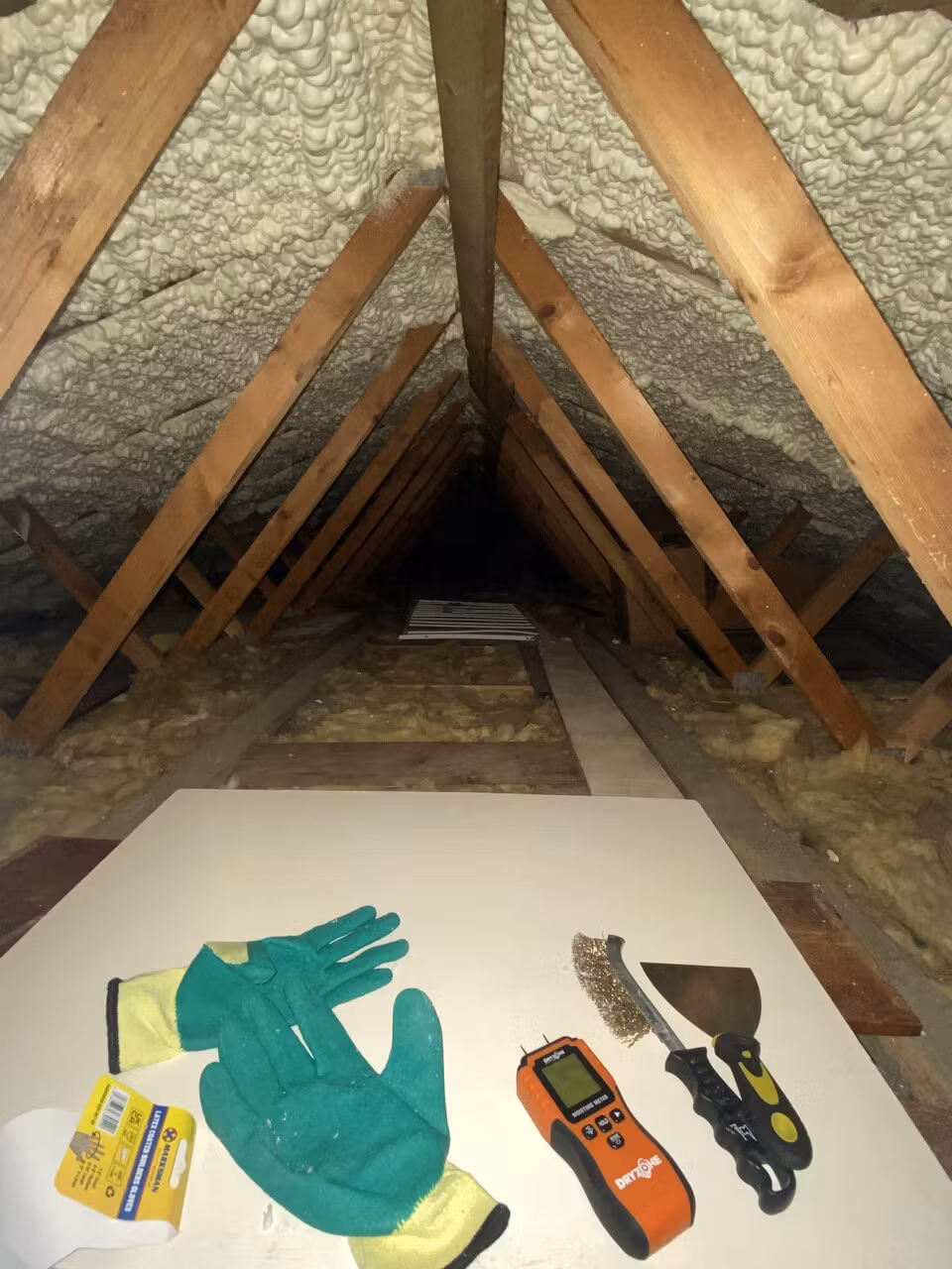 Gloves, a scraper and a moisture meter laid out in the loft